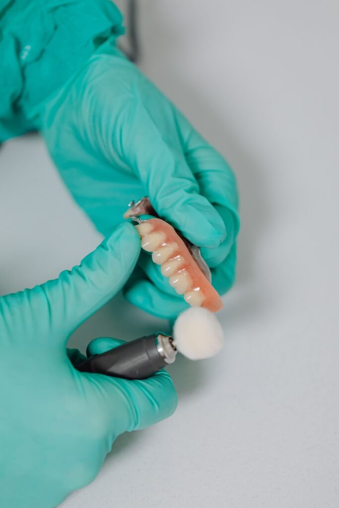 Dentist polishing dentures with rotary tool wearing green gloves in clinic.