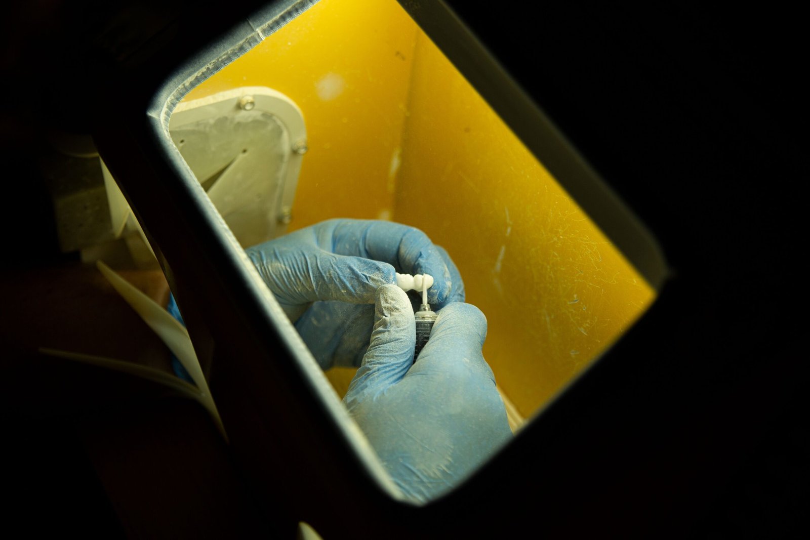 From above of crop anonymous master in latex gloves creating dental implant using medical equipment against black background
